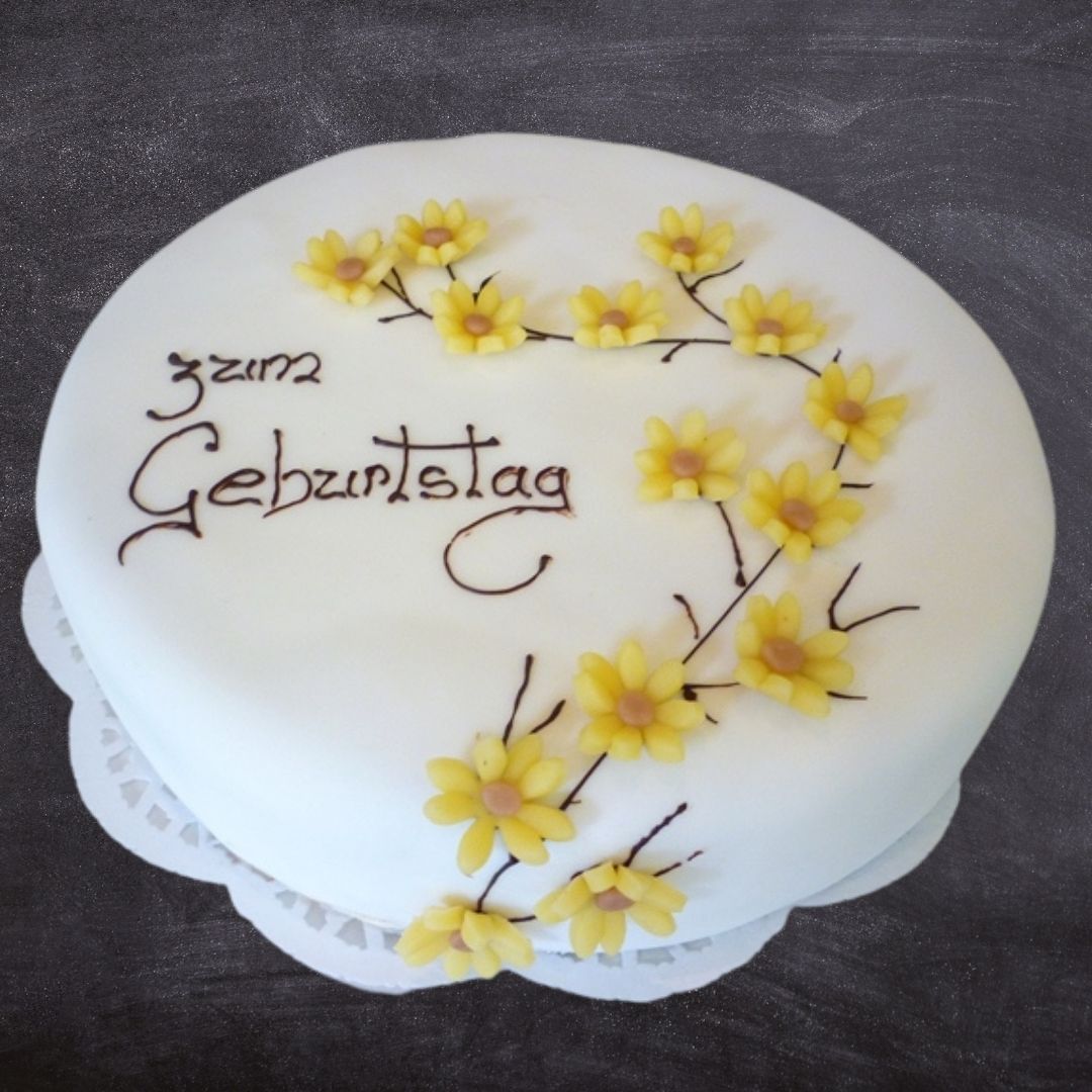 Elegante weiße Torte mit gelben Blüten zum Geburtstag. Handgemacht in der Conditorei froemmel's.