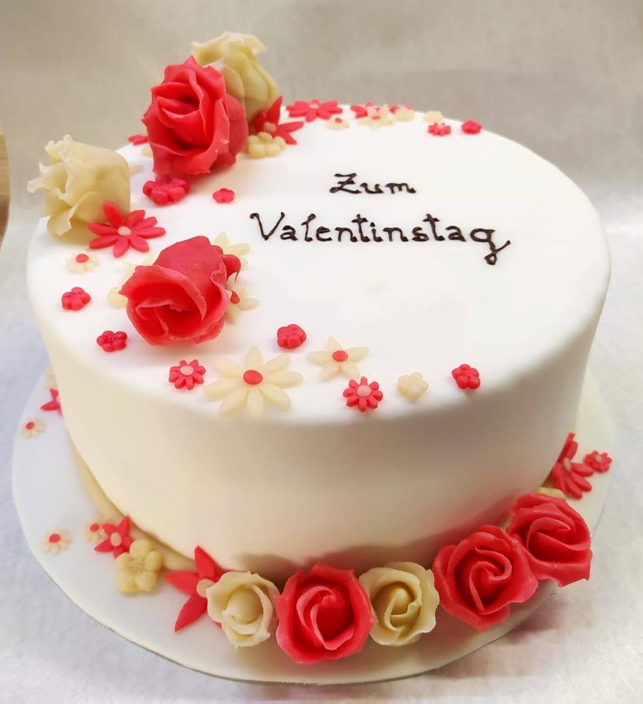 Die Torte zum Valentinstag wurde auf Wunsch mit weißem Fondant und cremefarbenen und korallenroten Blumen dekoriert.